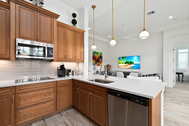 kitchen with pendant lighting, sink, light hardwood / wood-style flooring, appliances with stainless steel finishes, and kitchen peninsula