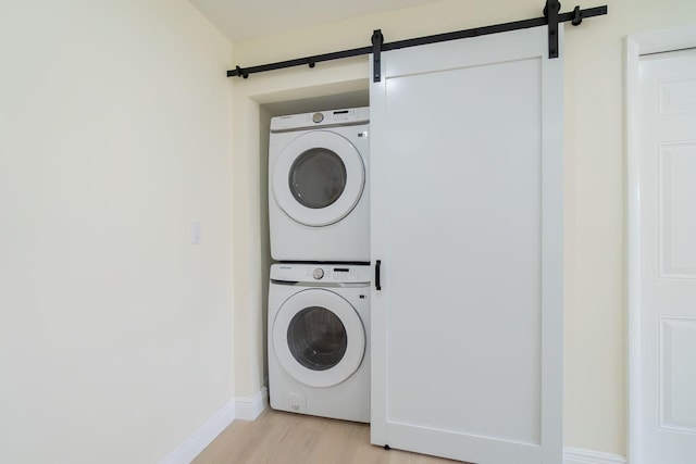 washroom with a barn door, stacked washing maching and dryer, and light hardwood / wood-style flooring