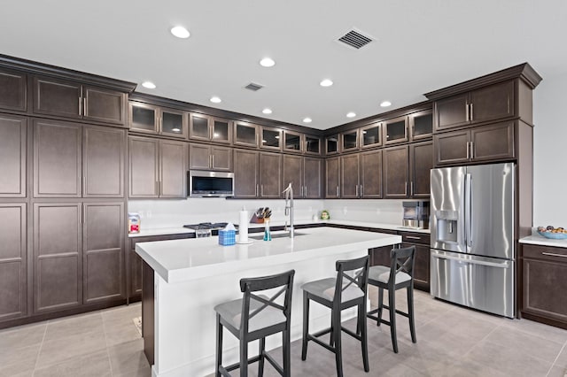 kitchen with appliances with stainless steel finishes, a center island with sink, dark brown cabinets, and sink