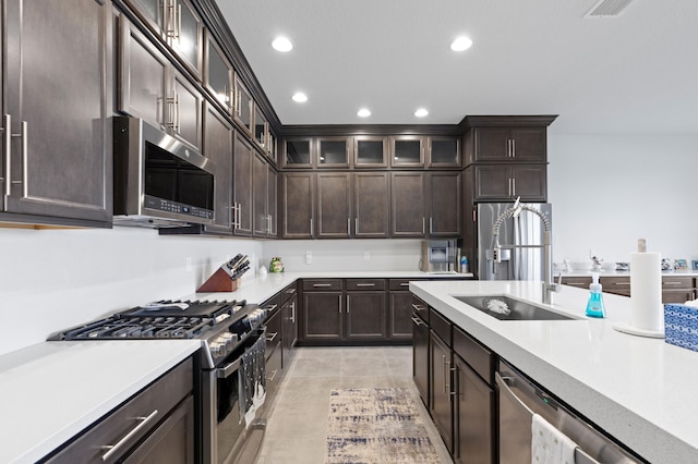 kitchen with light tile patterned flooring, dark brown cabinets, stainless steel appliances, and sink