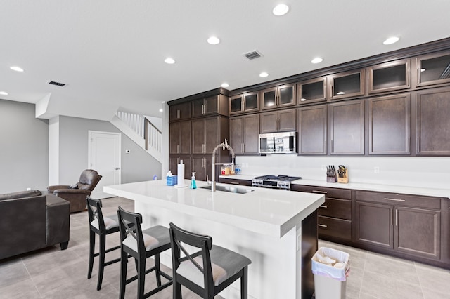 kitchen with sink, a breakfast bar area, an island with sink, dark brown cabinets, and stainless steel appliances