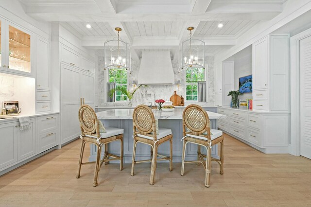 kitchen with coffered ceiling, white cabinetry, a center island, a kitchen breakfast bar, and pendant lighting