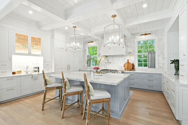 kitchen featuring light stone counters, hanging light fixtures, light wood-type flooring, a kitchen breakfast bar, and a kitchen island