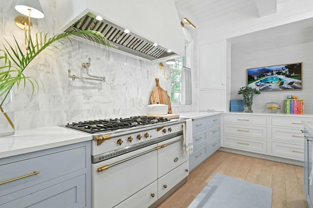 kitchen featuring backsplash, double oven range, light hardwood / wood-style floors, wall chimney range hood, and beam ceiling