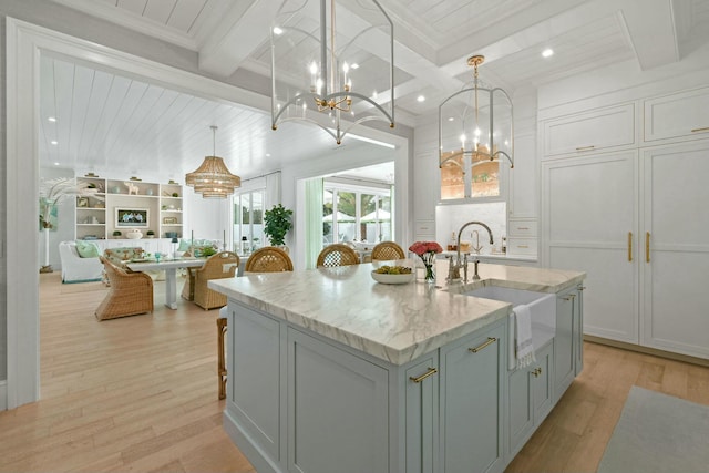 kitchen featuring decorative light fixtures, an island with sink, sink, light stone counters, and beam ceiling