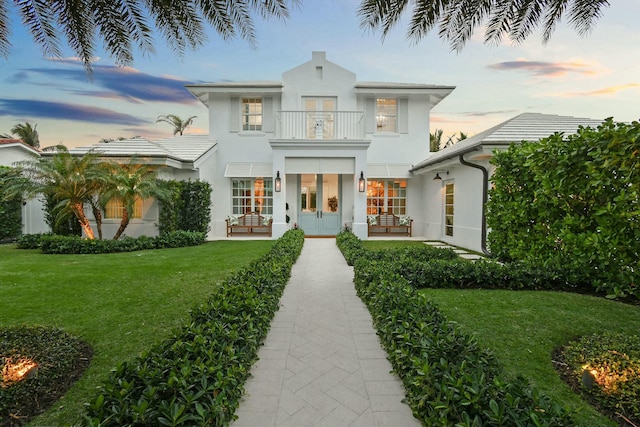 view of front of home with french doors, a balcony, and a lawn