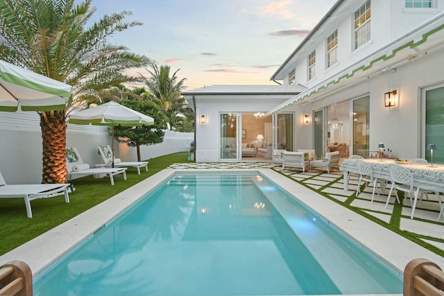 pool at dusk featuring a patio, outdoor lounge area, and a lawn