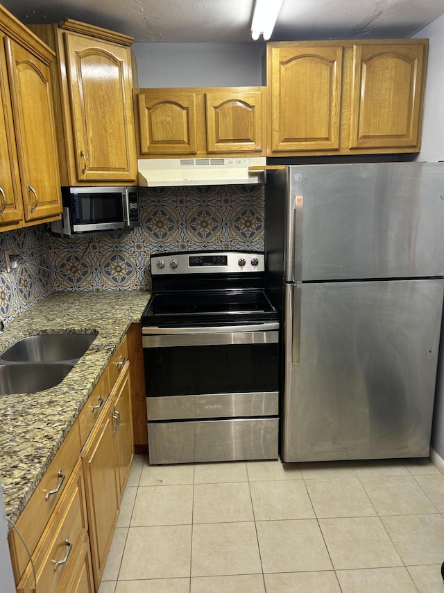 kitchen with tasteful backsplash, stainless steel appliances, sink, stone counters, and light tile patterned flooring