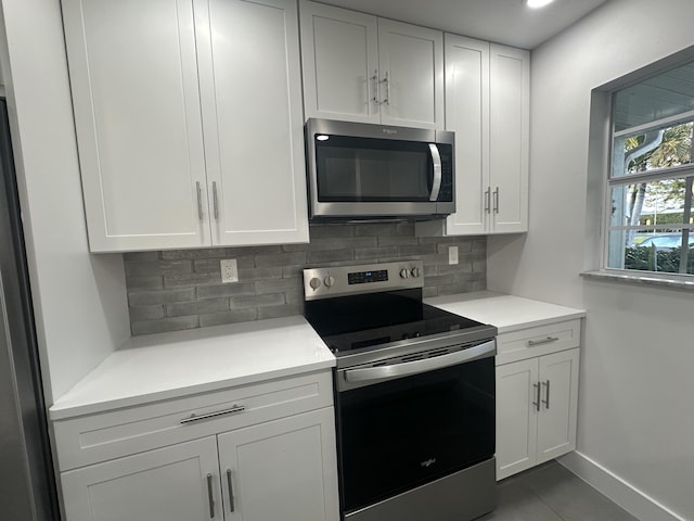 kitchen featuring appliances with stainless steel finishes, backsplash, white cabinetry, and dark tile patterned flooring