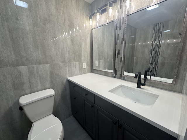 bathroom featuring a tile shower, vanity, tile walls, and toilet