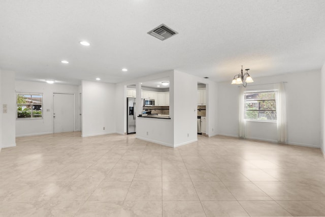 unfurnished living room with light tile patterned floors, a textured ceiling, a healthy amount of sunlight, and a notable chandelier