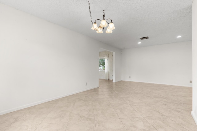 tiled empty room featuring a textured ceiling and an inviting chandelier