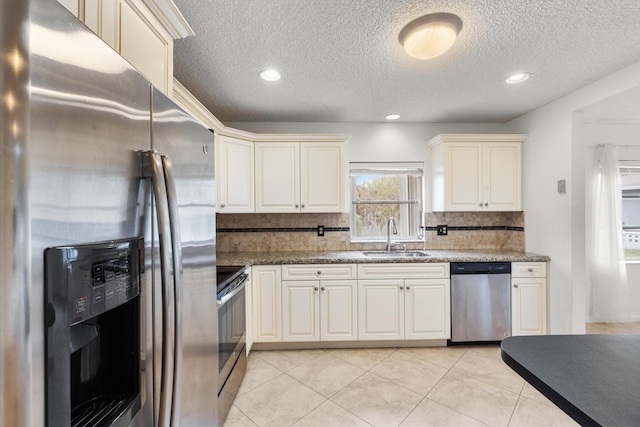 kitchen featuring sink, tasteful backsplash, dark stone countertops, cream cabinets, and appliances with stainless steel finishes