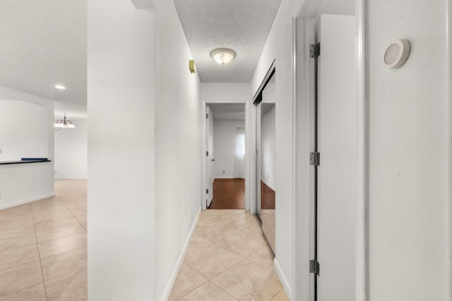 hallway with light tile patterned floors, a textured ceiling, and an inviting chandelier