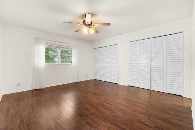 unfurnished bedroom featuring dark hardwood / wood-style flooring, two closets, and ceiling fan