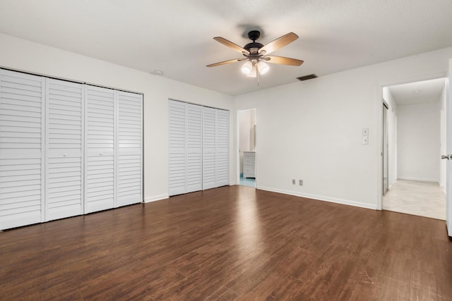 unfurnished bedroom with two closets, ceiling fan, and dark hardwood / wood-style floors