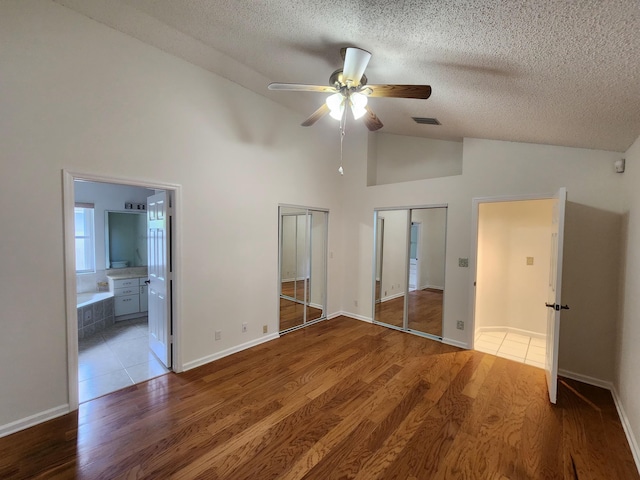 unfurnished bedroom featuring ensuite bath, ceiling fan, high vaulted ceiling, wood-type flooring, and a textured ceiling