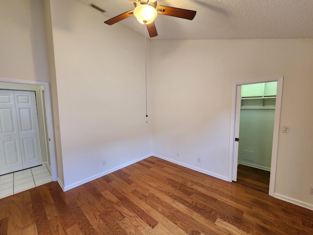 unfurnished bedroom featuring a textured ceiling, ceiling fan, a spacious closet, hardwood / wood-style floors, and a closet