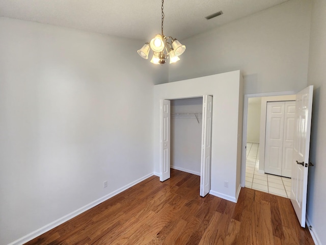 unfurnished bedroom with a closet, hardwood / wood-style floors, and a notable chandelier