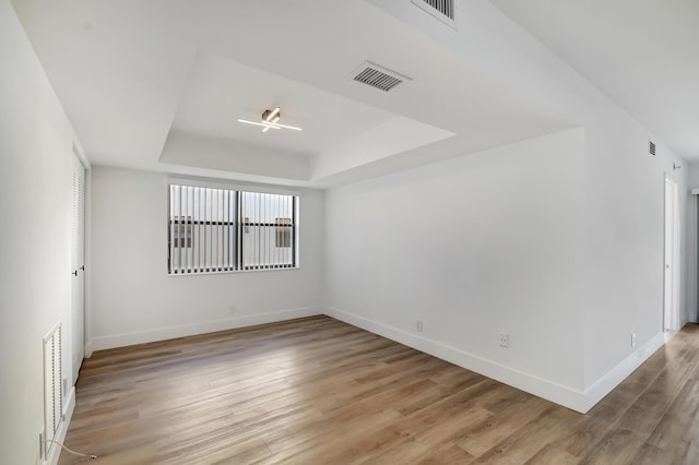 spare room featuring light hardwood / wood-style floors and a raised ceiling