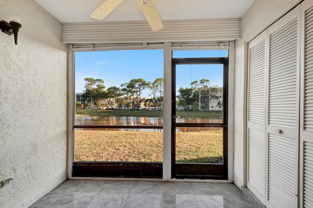 unfurnished sunroom featuring a water view, ceiling fan, and a healthy amount of sunlight