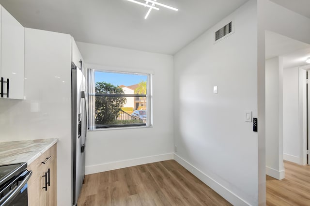 kitchen featuring light stone counters, white cabinetry, stainless steel appliances, and light hardwood / wood-style flooring