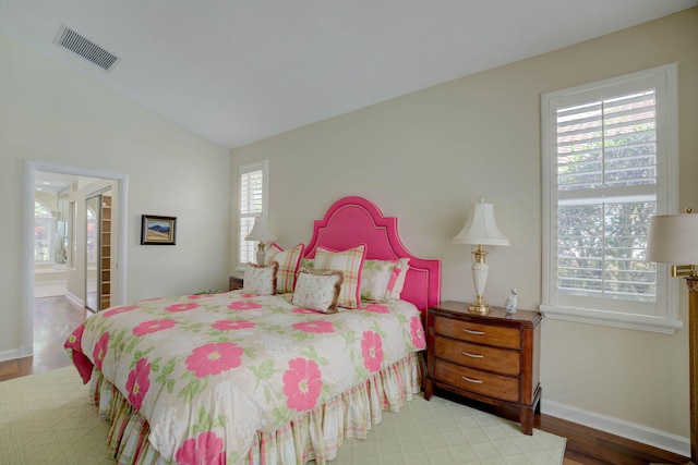 bedroom with ensuite bathroom, light hardwood / wood-style floors, and lofted ceiling