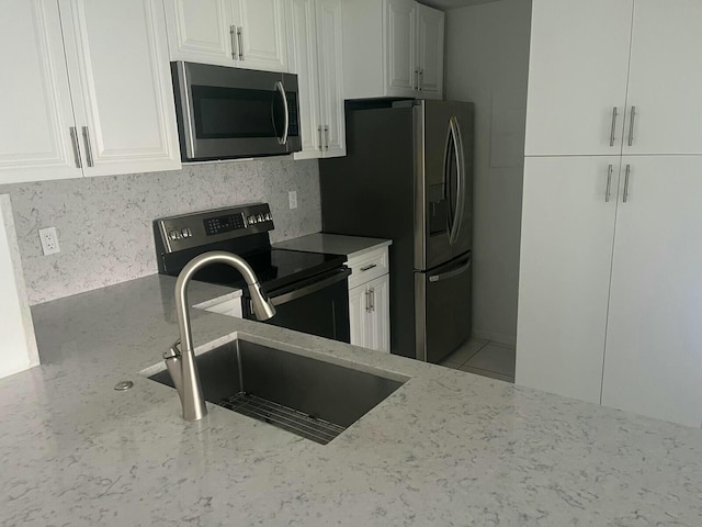 kitchen featuring stainless steel appliances, a sink, white cabinets, light stone countertops, and tasteful backsplash