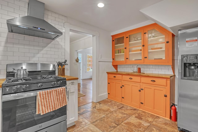 kitchen featuring tasteful backsplash, butcher block counters, wall chimney exhaust hood, and appliances with stainless steel finishes