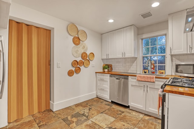 kitchen with wooden counters, decorative backsplash, stainless steel dishwasher, gas range, and white cabinets