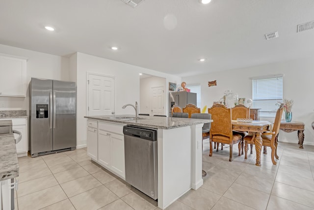 kitchen with sink, light tile patterned floors, appliances with stainless steel finishes, a kitchen island with sink, and white cabinets