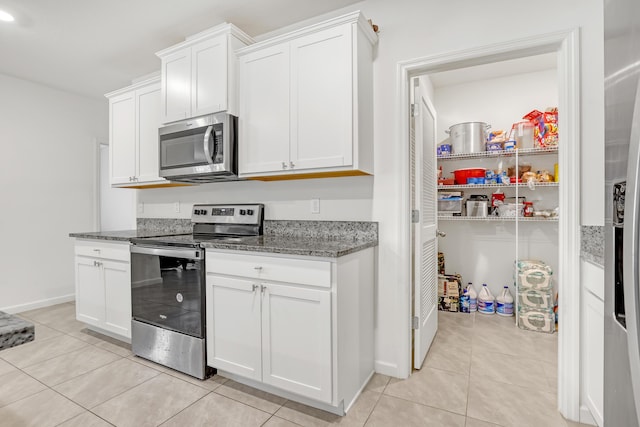 kitchen featuring white cabinetry, stainless steel appliances, light tile patterned floors, and dark stone counters