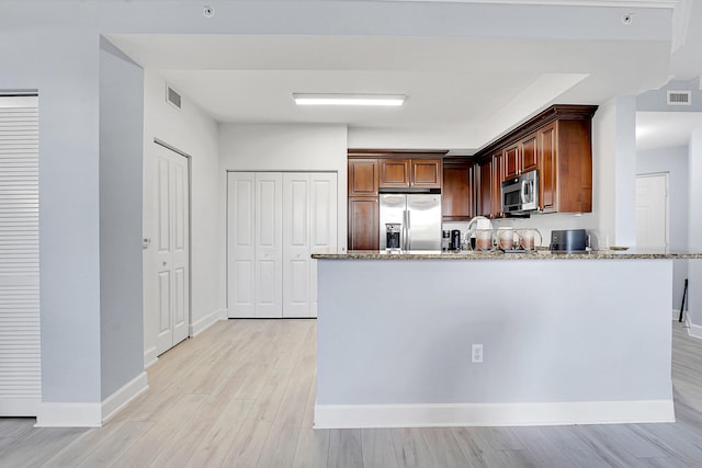 kitchen with light stone countertops, appliances with stainless steel finishes, kitchen peninsula, and light hardwood / wood-style flooring