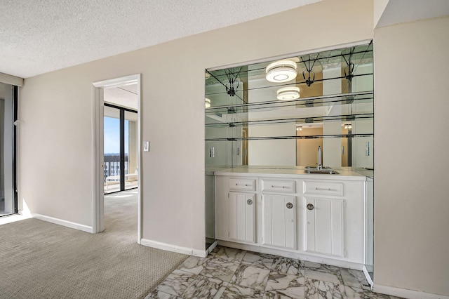 bar featuring sink, white cabinets, light colored carpet, and a textured ceiling