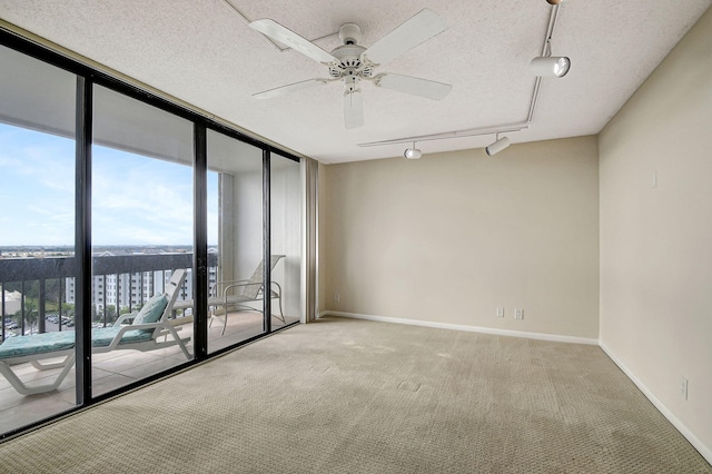 empty room with ceiling fan, a wall of windows, a textured ceiling, and track lighting