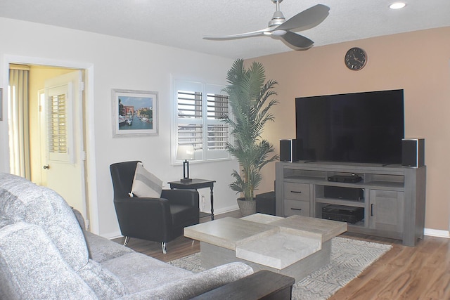 living area with a textured ceiling, light wood-type flooring, a ceiling fan, and baseboards