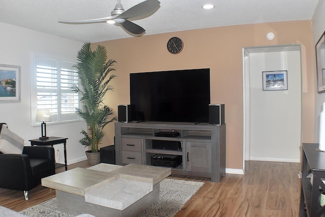 living area with light wood-style floors, a textured ceiling, baseboards, and a ceiling fan