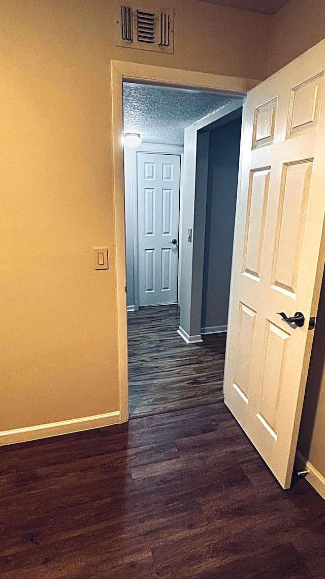 hall featuring dark wood-style floors, visible vents, and baseboards