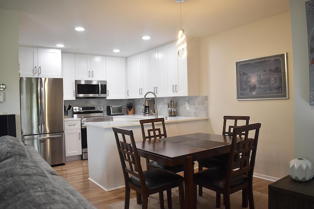 kitchen featuring light wood-style floors, white cabinets, appliances with stainless steel finishes, tasteful backsplash, and decorative light fixtures