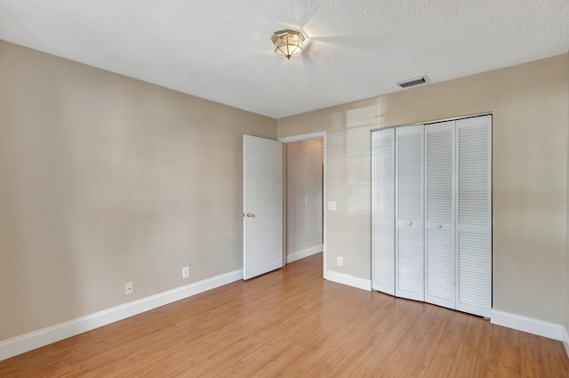 unfurnished bedroom with a textured ceiling, light hardwood / wood-style flooring, and a closet