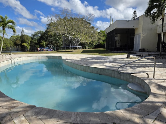 outdoor pool with a patio area, a trampoline, a lawn, and fence