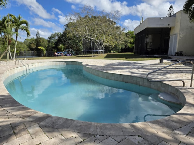 outdoor pool featuring a trampoline, a lawn, and fence