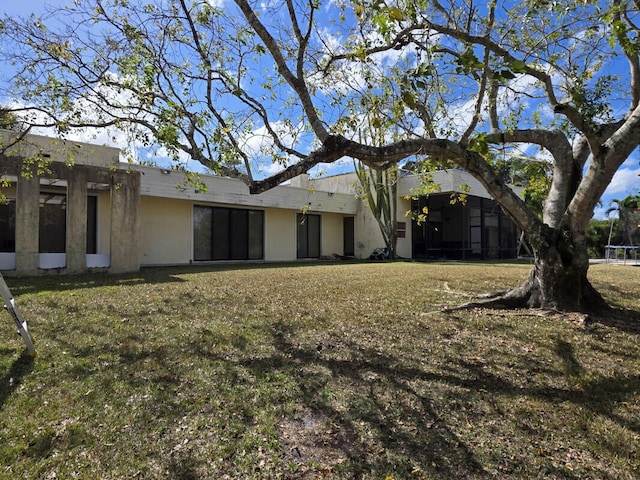 back of property with a trampoline and a yard