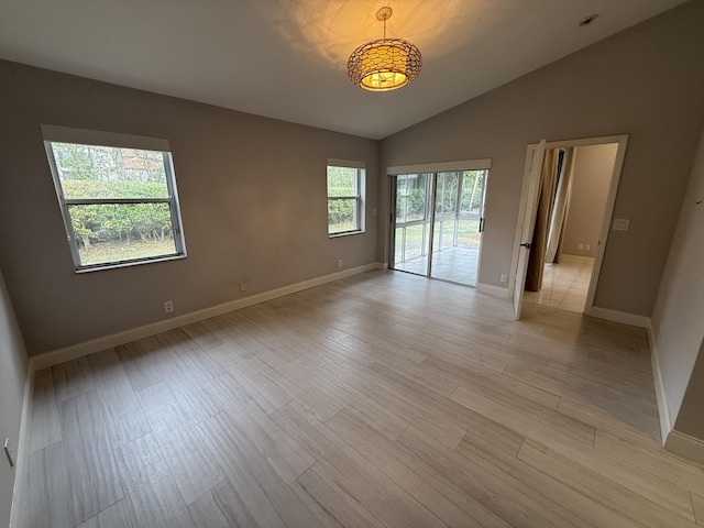 empty room featuring lofted ceiling, a healthy amount of sunlight, and light wood-type flooring