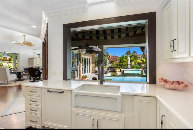 kitchen with ceiling fan, sink, white cabinets, and ornamental molding