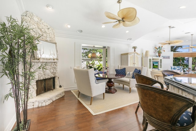 living room featuring ceiling fan, dark wood-type flooring, crown molding, a stone fireplace, and lofted ceiling