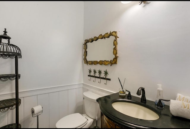 half bathroom featuring vanity, toilet, a wainscoted wall, and a decorative wall