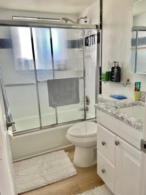 full bathroom featuring vanity, hardwood / wood-style flooring, toilet, and bath / shower combo with glass door