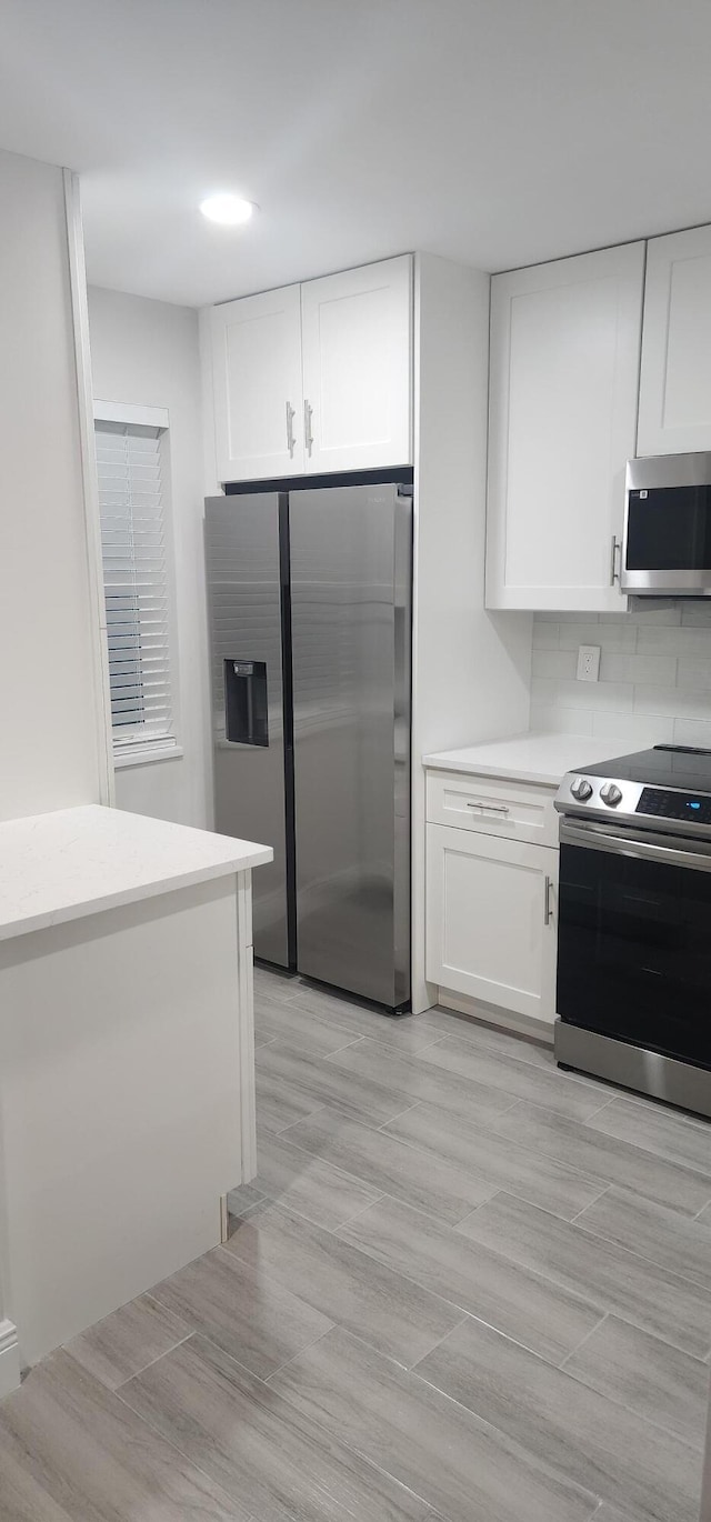 kitchen featuring white cabinets, light hardwood / wood-style floors, stainless steel appliances, and tasteful backsplash