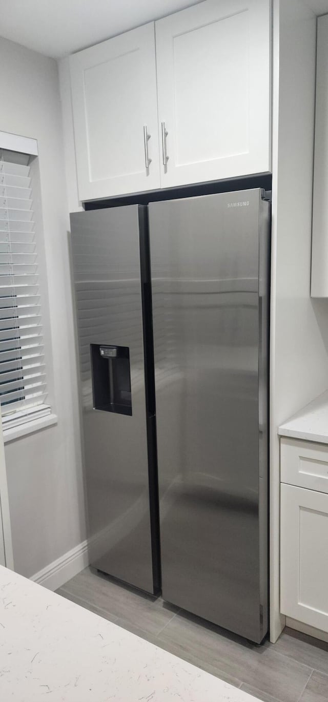 interior space featuring stainless steel fridge with ice dispenser, light wood-type flooring, and white cabinetry